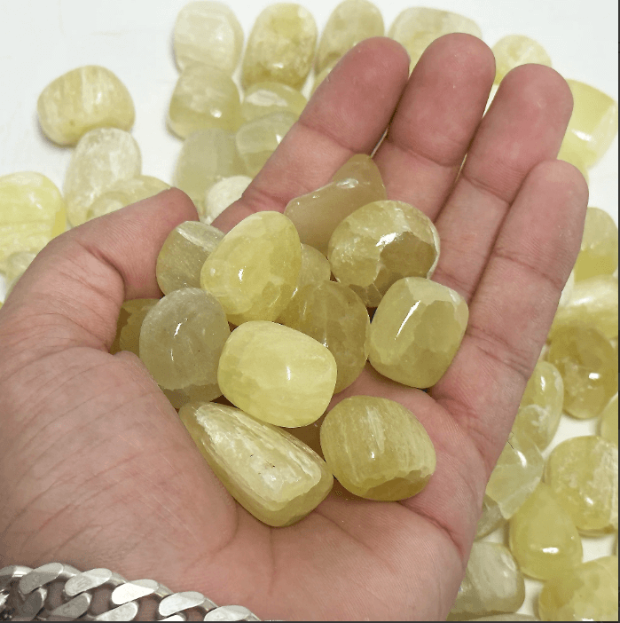 Hand holding genuine lemon quartz tumbled stones, showcasing their bright yellow clarity and natural beauty.